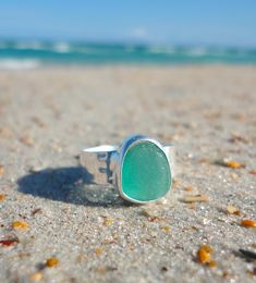 a green sea glass ring sitting on top of a sandy beach next to the ocean