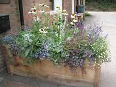 a wooden planter filled with lots of purple and white flowers next to a brick building