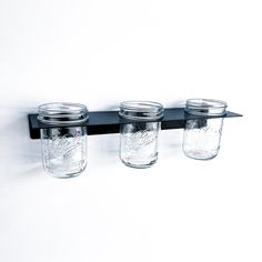 three mason jars are hanging on a black shelf with glass lids and metal bar handles