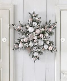 a christmas wreath hanging on the side of a white door with silver and pink ornaments