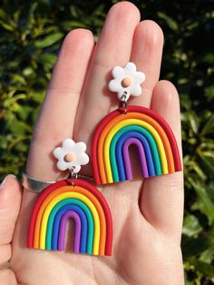 a hand holding two rainbow earrings with flowers on each one and a flower in the middle