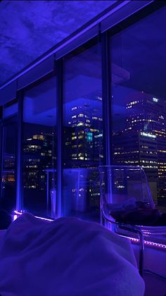 a bedroom with a view of the city lights at night and purple lighting on the walls