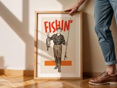 a man standing next to a fishin poster on the wall with his feet propped up