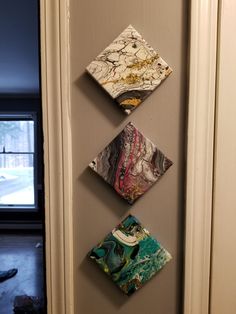 three square shaped artwork hanging on the wall next to a door with an open window