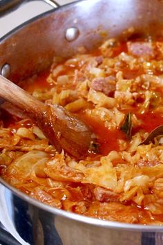 a large pot filled with lots of food on top of a stove next to a wooden spoon