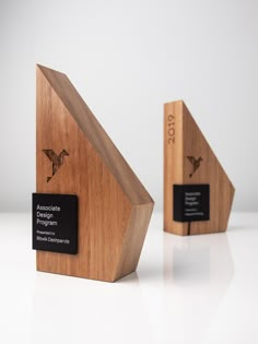 two wooden trophies with black labels on them sitting next to each other in front of a white background