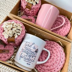 two pink coffee mugs in a box with some crochet coasters on them