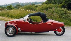 an old fashioned red car is parked on the side of the road in front of some bushes