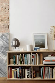 a bookshelf filled with lots of books next to a brick wall and lamp