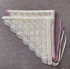 a white crocheted triangle with pink thread on it's end and two strings hanging from the side