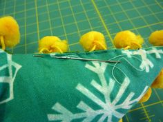 some yellow pom poms are on top of a green fabric with white snowflakes