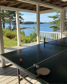 an outdoor ping pong table on the porch with water and trees in the background