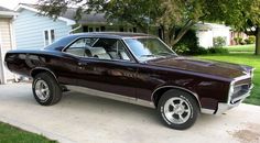 a purple muscle car parked in front of a house on a driveway next to a tree