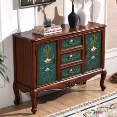 a sideboard with flowers painted on it in front of a painting and vases