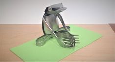 a metal bird sculpture sitting on top of a green piece of paper next to a knife and fork