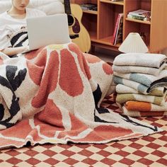 a woman is sitting on the floor working on her laptop while she sits in bed