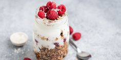 a glass jar filled with granola, raspberries and yogurt next to a spoon