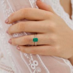 a woman wearing a ring with an emerald stone