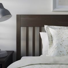 a bed with white sheets and pillows next to a lamp on the side of the headboard