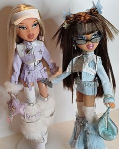 two dolls standing next to each other on top of a table with one holding a purse