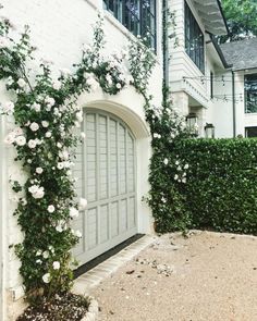 a white house with roses growing on the side and an arched door that leads to another building