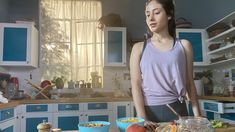 a woman standing in a kitchen next to a table filled with bowls and food items