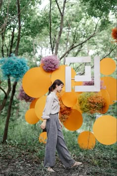 a woman is walking in the woods with balloons and flowers hanging from her head as she walks by herself