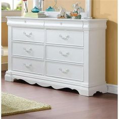 a white dresser sitting in a room next to a rug on the floor and a mirror above it