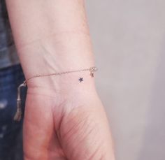 a person wearing a tiny star tattoo on their left wrist with a tassel attached to it