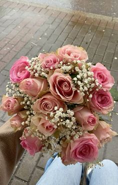 a bouquet of pink roses sitting on the back of a person's lap in front of a brick sidewalk