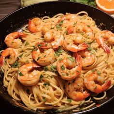 pasta with shrimp and parsley in a skillet on a table next to an orange slice