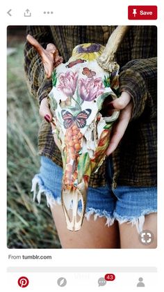 a woman holding a cow skull with flowers painted on it