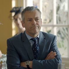 a man in a suit and tie standing with his arms crossed looking at the camera