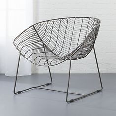 a wire chair sitting on top of a gray floor next to a white brick wall