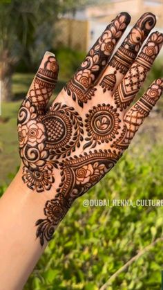 a hand with henna on it and green plants in the backgroung