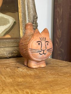 a cat figurine sitting on top of a wooden table next to a painting