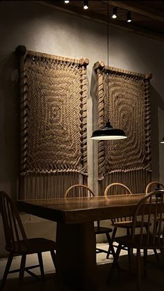 two wooden chairs sitting at a table in front of a large woven wall hanging on the wall