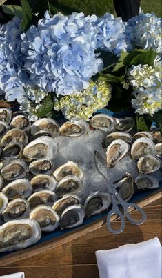 a table topped with lots of oysters next to blue hydrangeas and white flowers