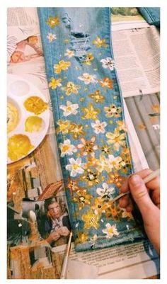 someone is painting flowers on an old pair of jean pants with yellow and white paint