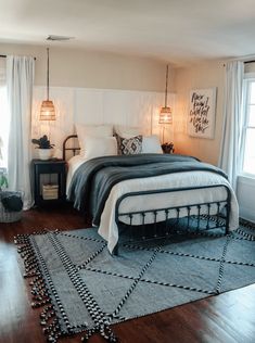 a bed sitting on top of a wooden floor next to two windows in a bedroom