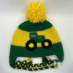 a green and yellow knitted hat with a tractor on the front, sitting on top of a white surface