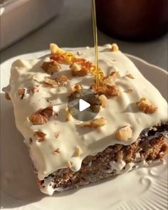 a white plate topped with a piece of cake covered in frosting and walnuts