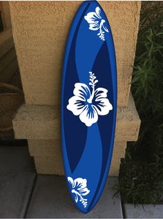 a blue and white surfboard sitting on the side of a building next to plants