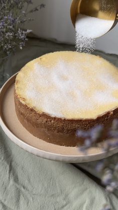 someone is sprinkling sugar on top of a cake with flowers in the background