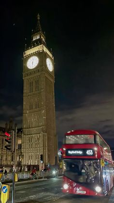 a red double decker bus driving past the big ben clock tower in london at night