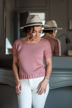 a woman standing in front of a mirror wearing white pants and a pink sweater with ruffles