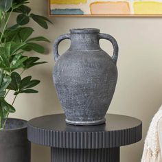 a gray vase sitting on top of a table next to a potted plant