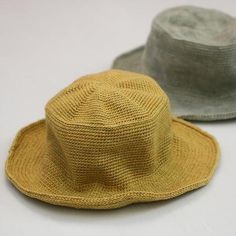 two hats sitting next to each other on top of a white table with one wearing a yellow hat