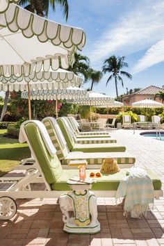 a row of lawn chairs sitting under an umbrella next to a swimming pool and palm trees