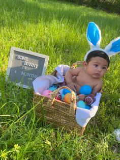 a baby wearing bunny ears sitting in a basket next to an easter egg hunt sign